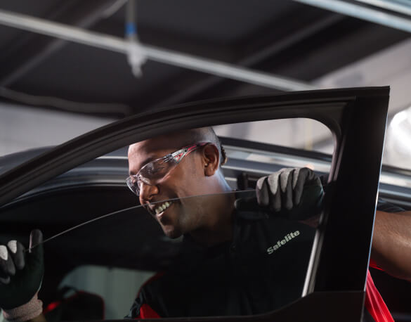 A Safelite technician wearing gloves replacing a vehicle's side window